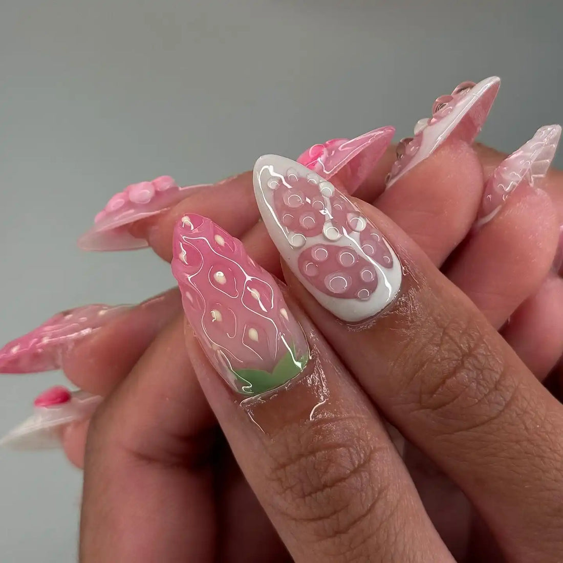 Hand with long pink press-on nails featuring 3D fruit designs including strawberries and cherries