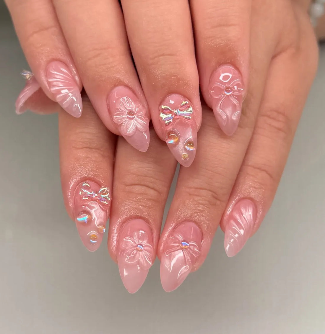 Handmade pink press-on nails with 3D iridescent bows and floral designs