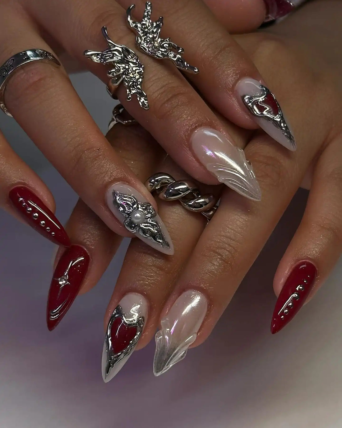 Hand with long stiletto press-on nails, red and pearl chrome with gothic heart and 3D accents.