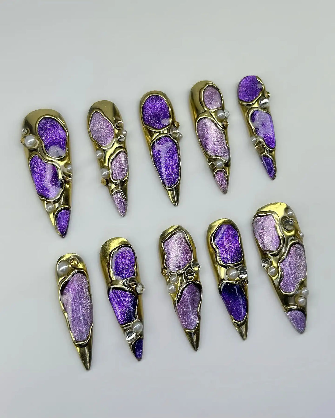 Handmade press-on nails with purple and gold chrome finish, iridescent accents, and pearls.