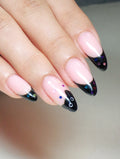 Hand with almond-shaped press-on nails featuring black French tips, colorful star accents, and a cute black cat design.