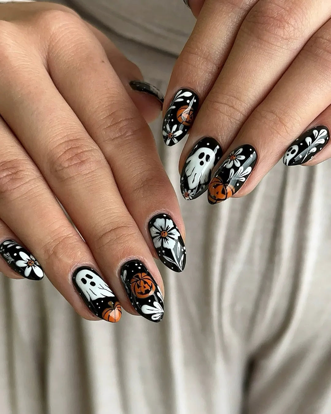 Handmade black press-on nails with white floral, ghost, and pumpkin Halloween designs.