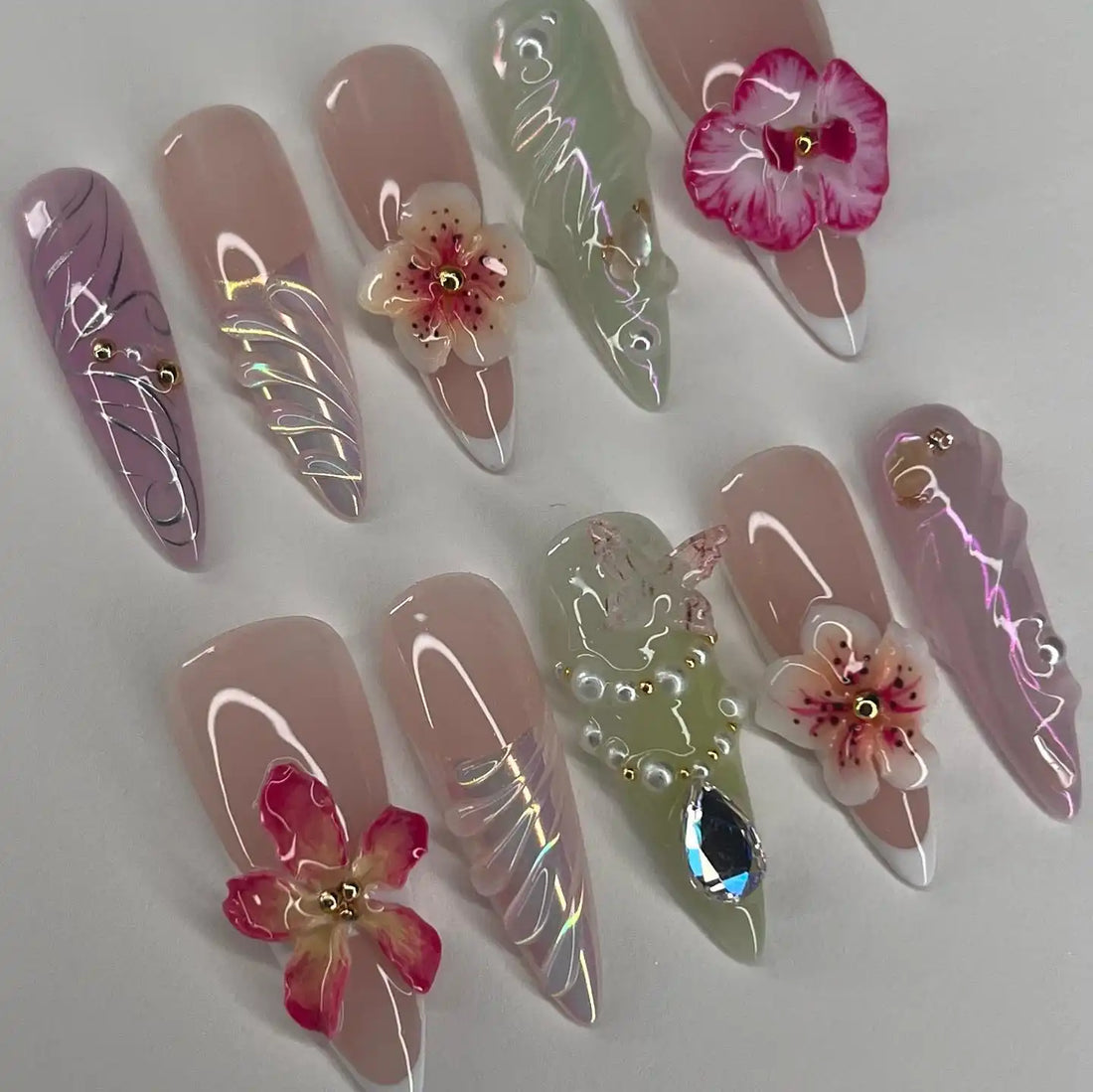 Handmade press-on nails with 3D flowers, pearls, glitter, and marble designs, arranged on a white background.