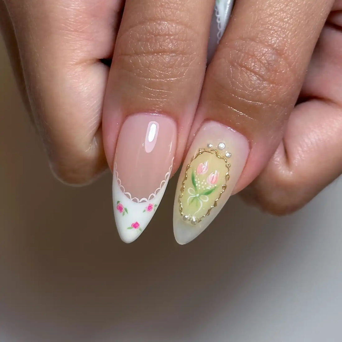 Hand with long almond-shaped press-on nails featuring pink strawberry French tips, bows, floral art, and 3D accents.