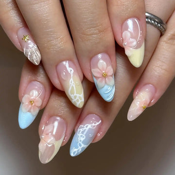 Hand with pastel blue and yellow seashell press-on nails featuring 3D floral designs