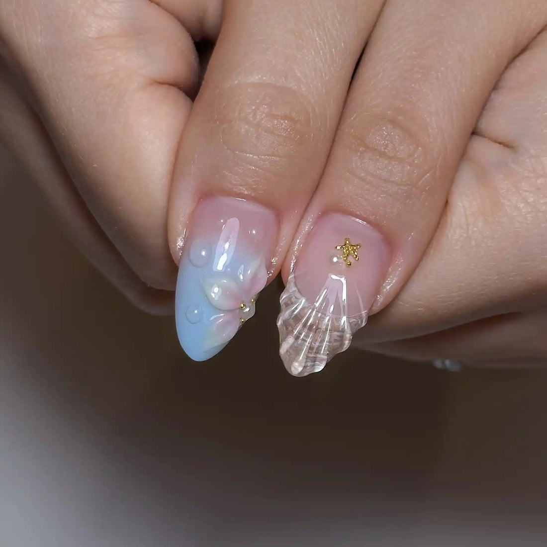 Hand with pastel blue and yellow seashell press-on nails featuring 3D floral designs