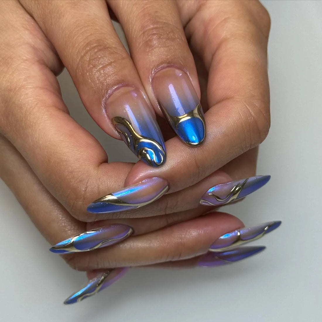 Hand with long coffin-shaped press-on nails in metallic blue with chrome abstract accents