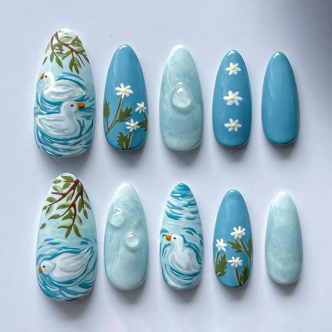 Handmade blue press-on nails with duck pond, white daisies, and spring art designs.