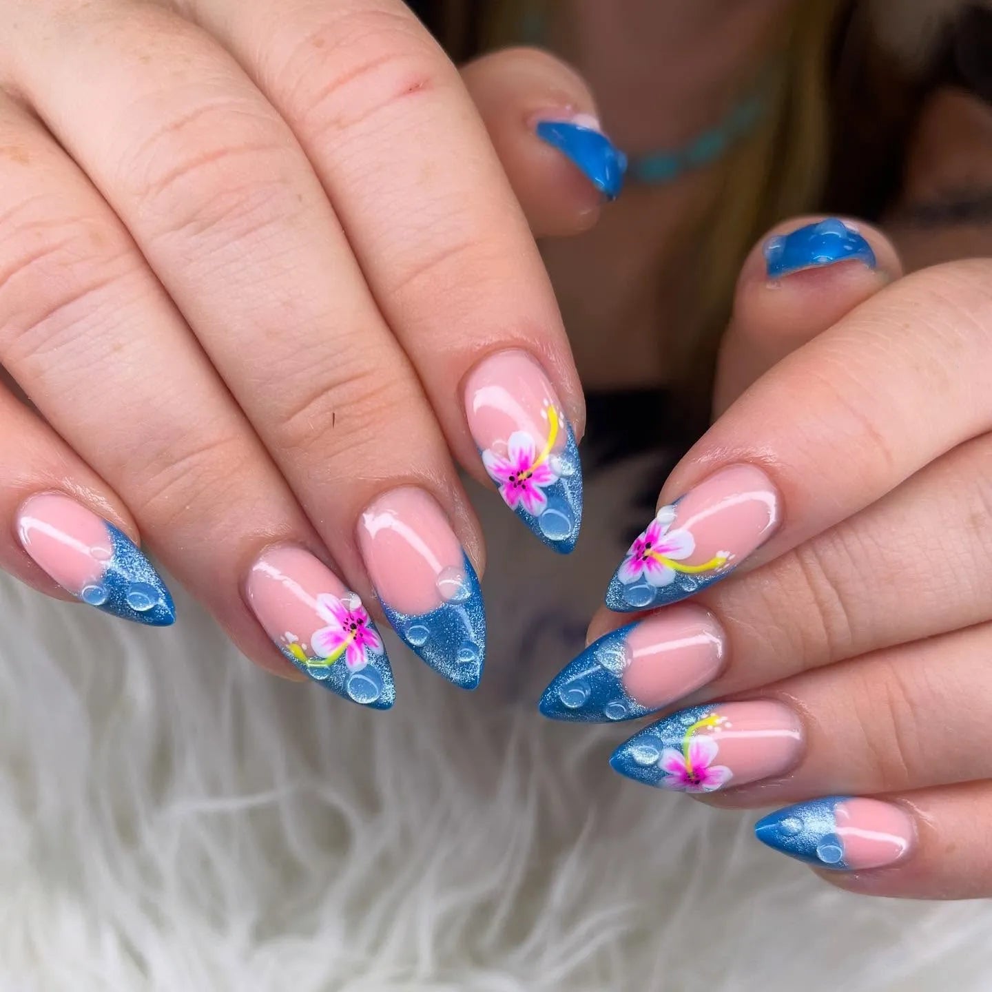 Hand with almond-shaped blue glitter hibiscus floral press-on nails and water droplet design