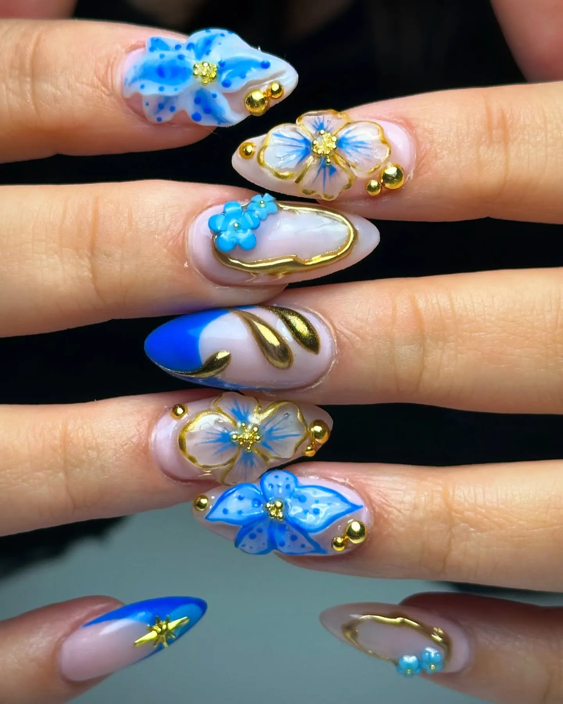 Hand with blue and gold floral 3D press-on nails, featuring bohemian luxe design.