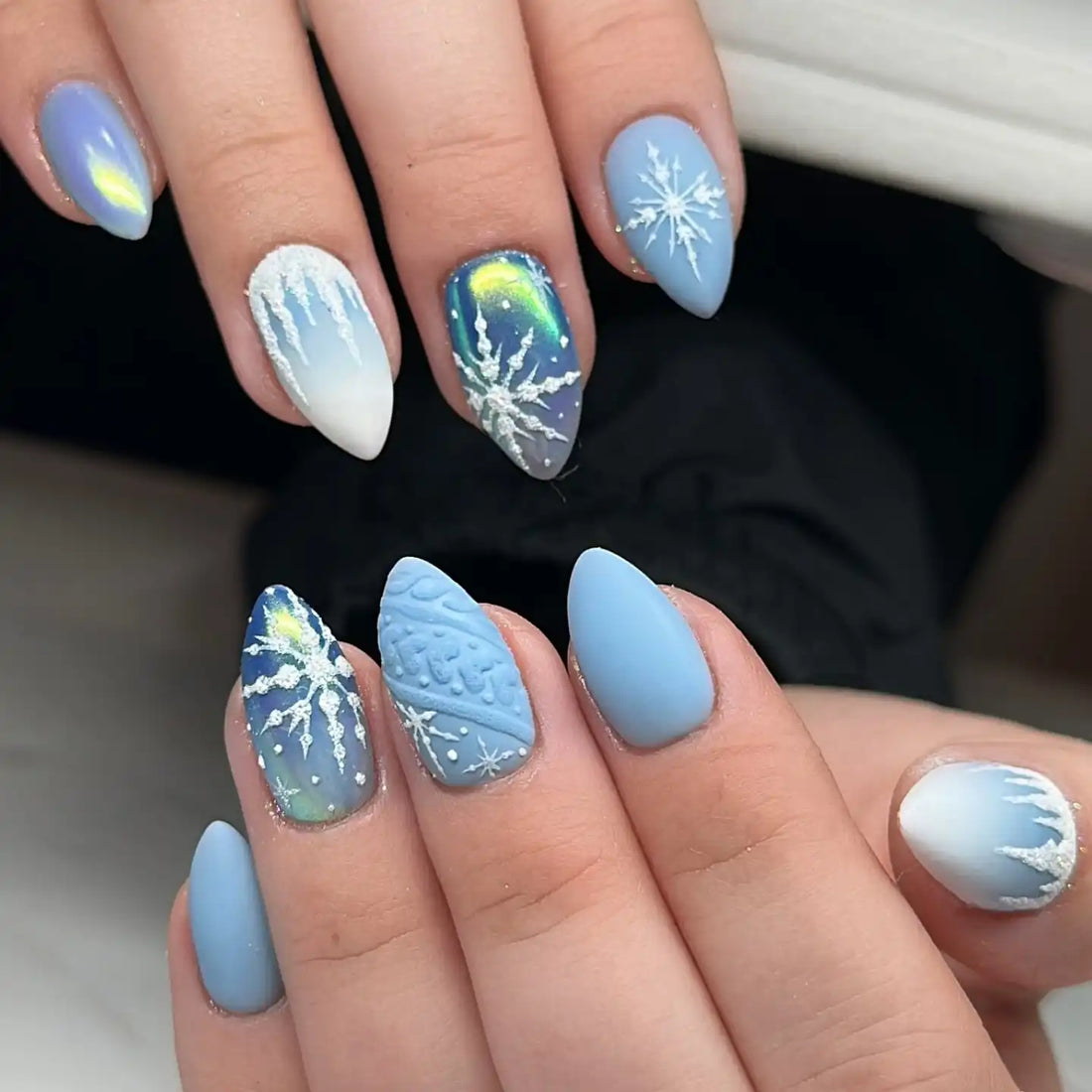 Handmade press-on nails with blue and white winter snowflake and icicle designs.
