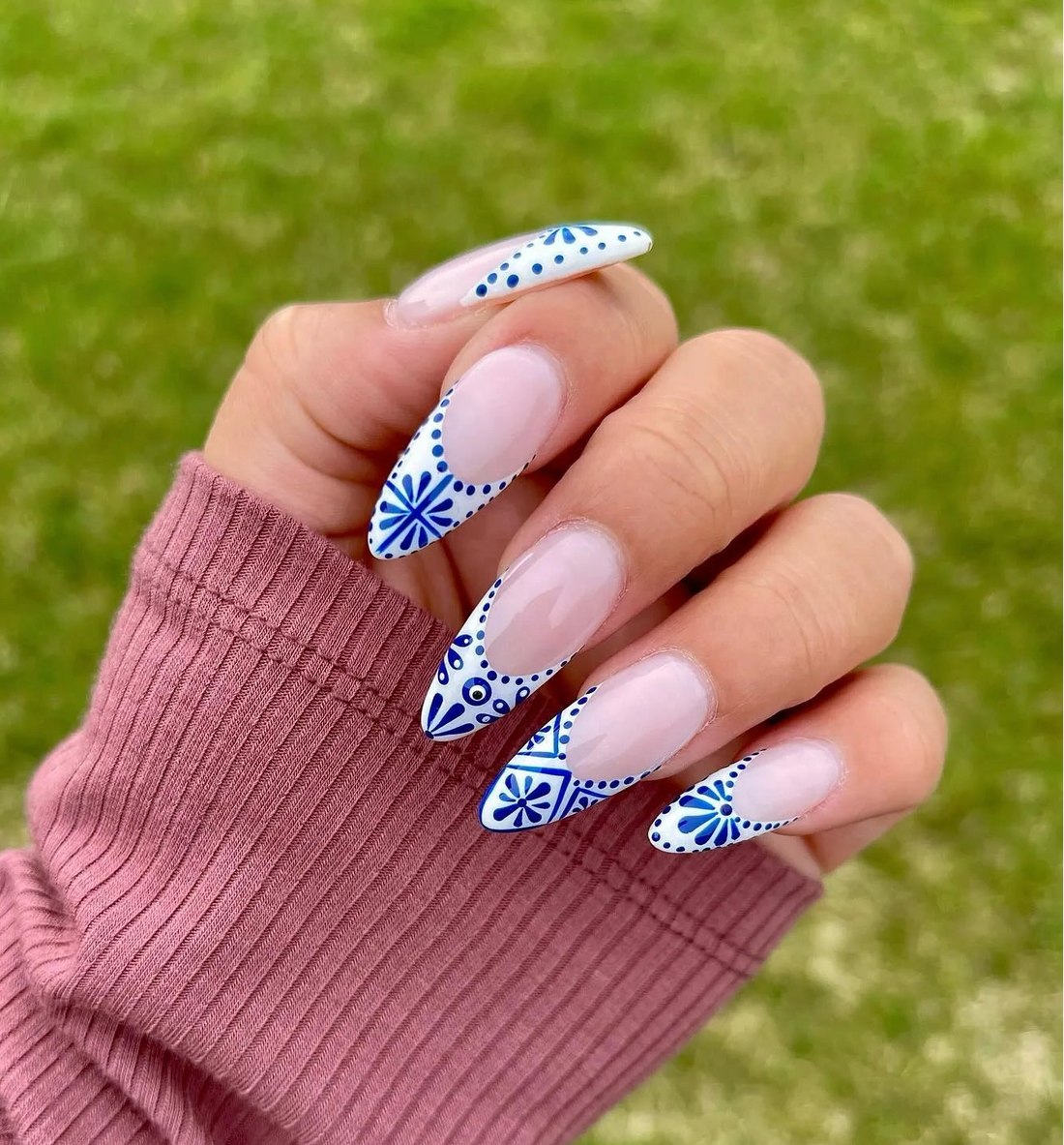 Hand wearing long handmade press-on nails with blue and white French tip tile pattern design.