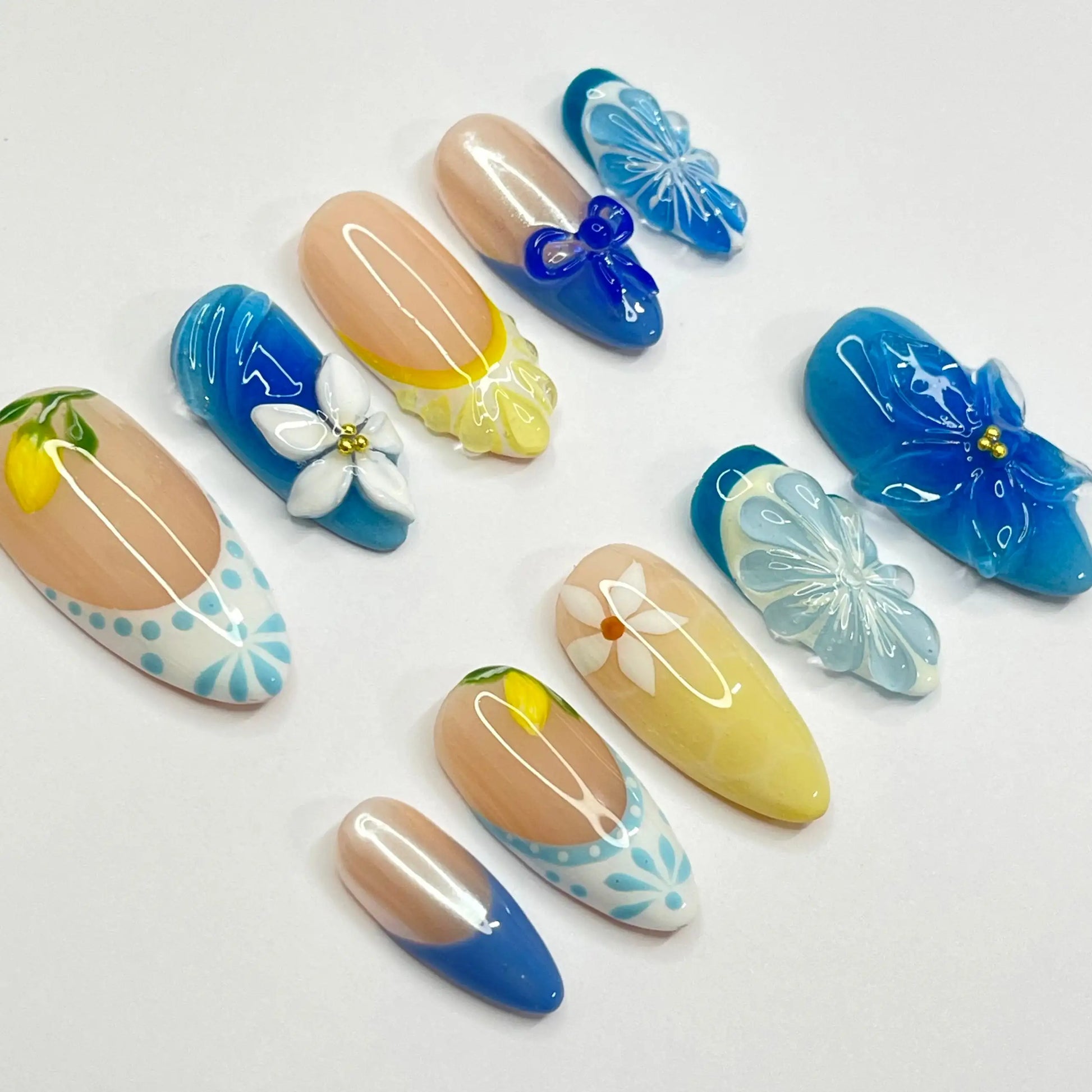 Handmade blue and yellow floral press-on nails with 3D lemon and flower designs on white background