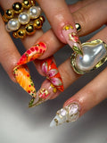 Hand with bold red, orange, and gold 3D floral butterfly press-on nails, luxury design.
