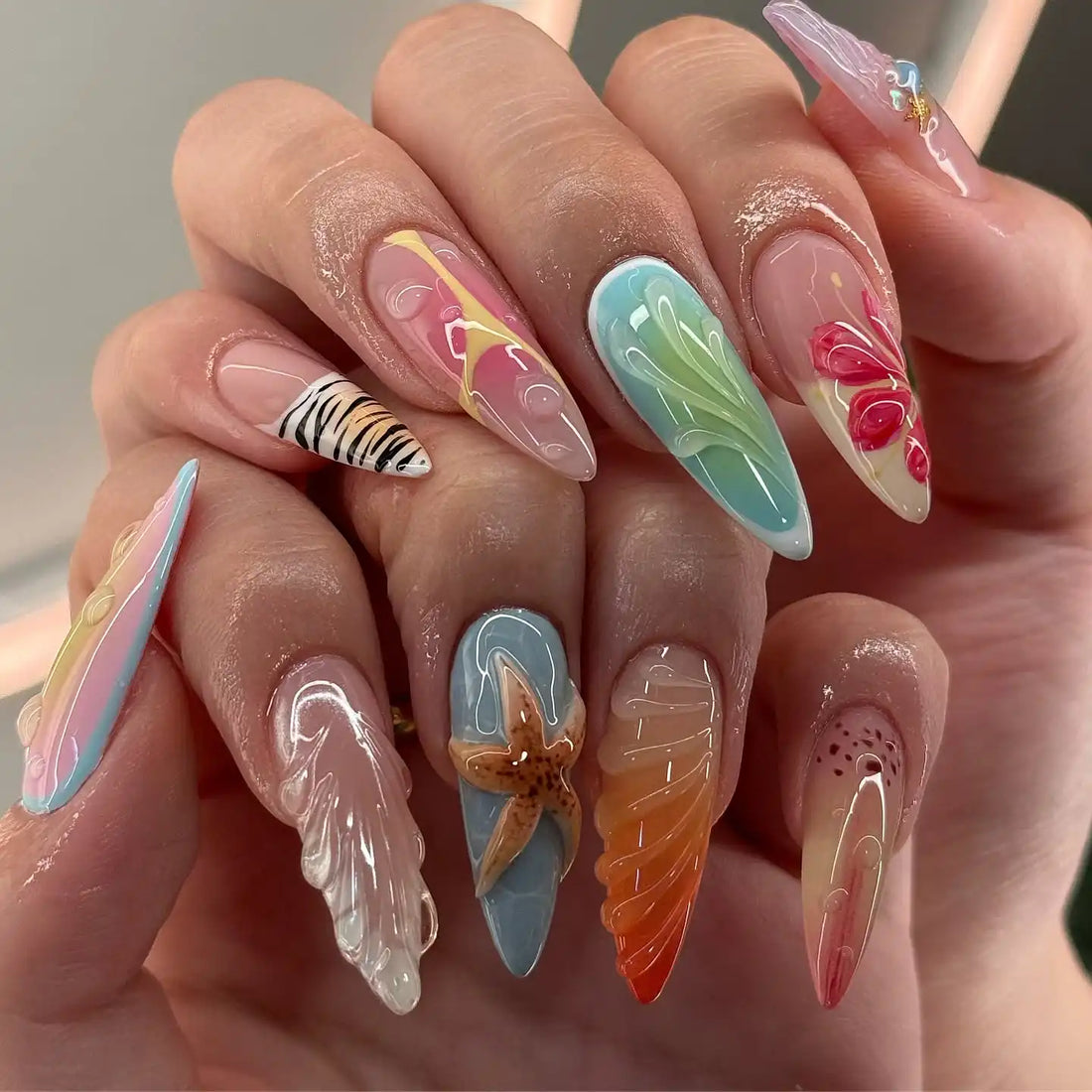 Hand with long handmade summer press-on nails featuring starfish, seashell, and colorful designs