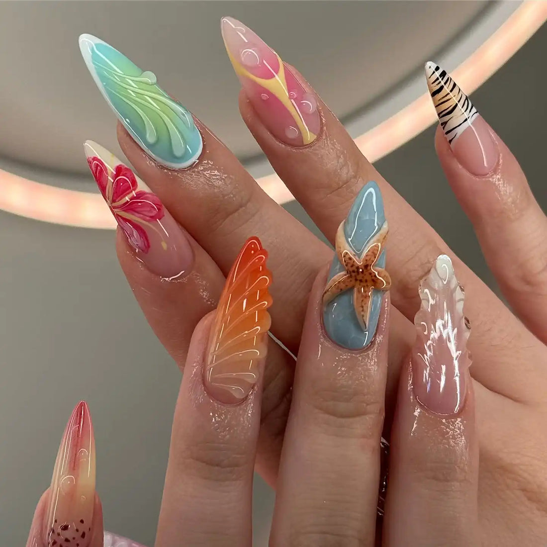 Hand with long handmade summer press-on nails featuring starfish, seashell, and colorful designs