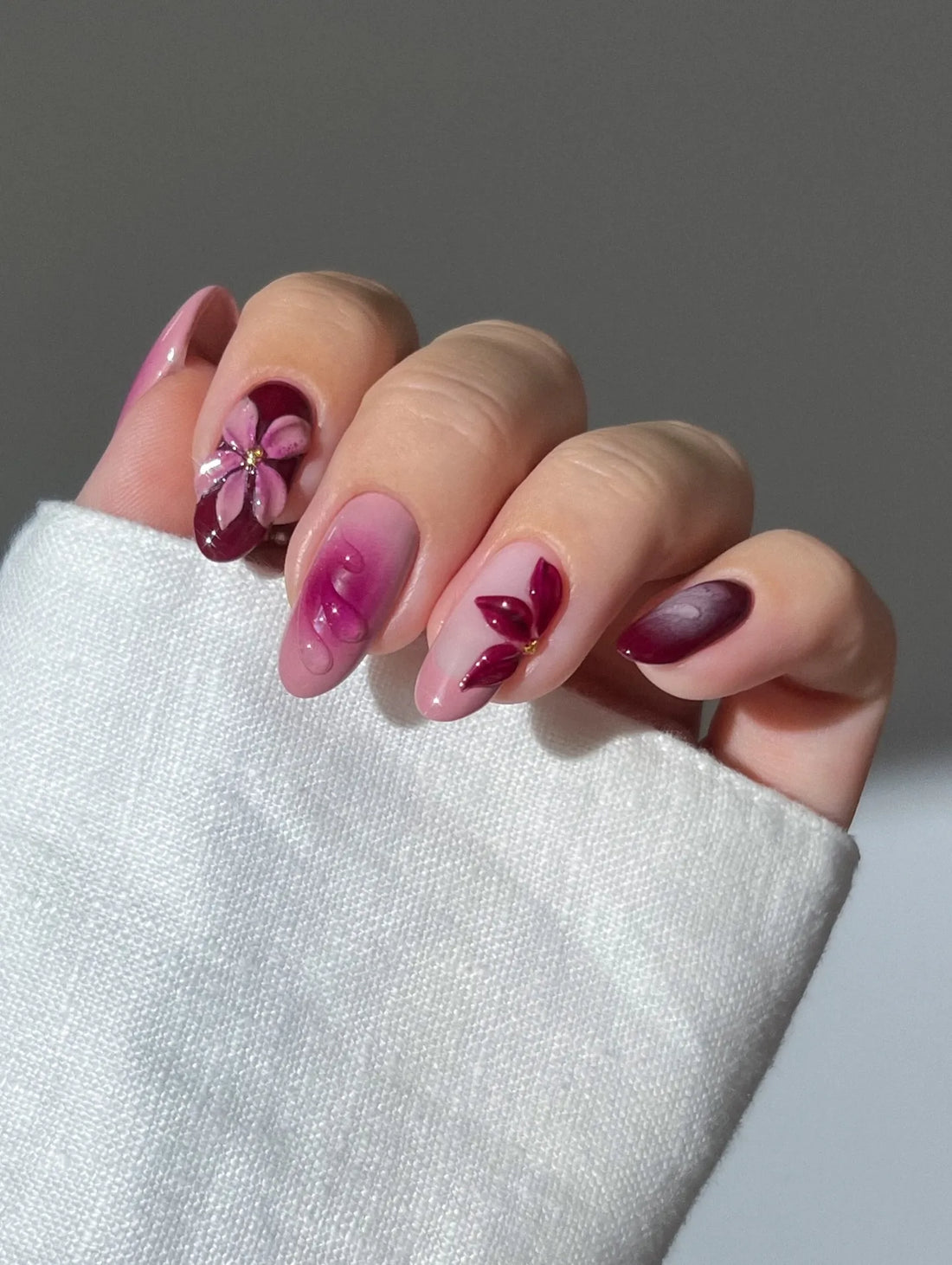 Hand with handmade burgundy and pink ombre press-on nails featuring 3D floral designs.