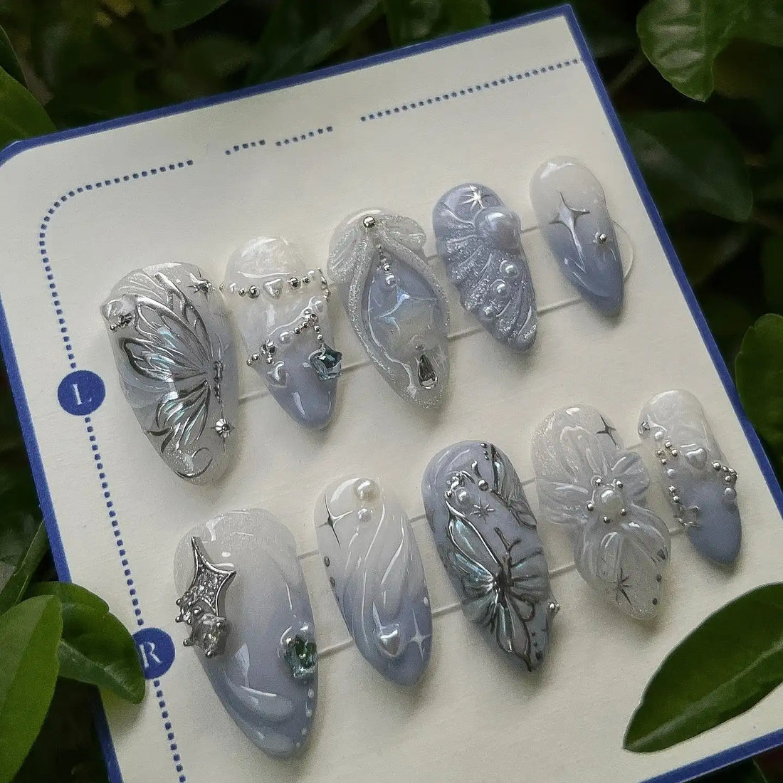 Handmade press-on nails with pearl, butterfly, moon, and star designs on iridescent base