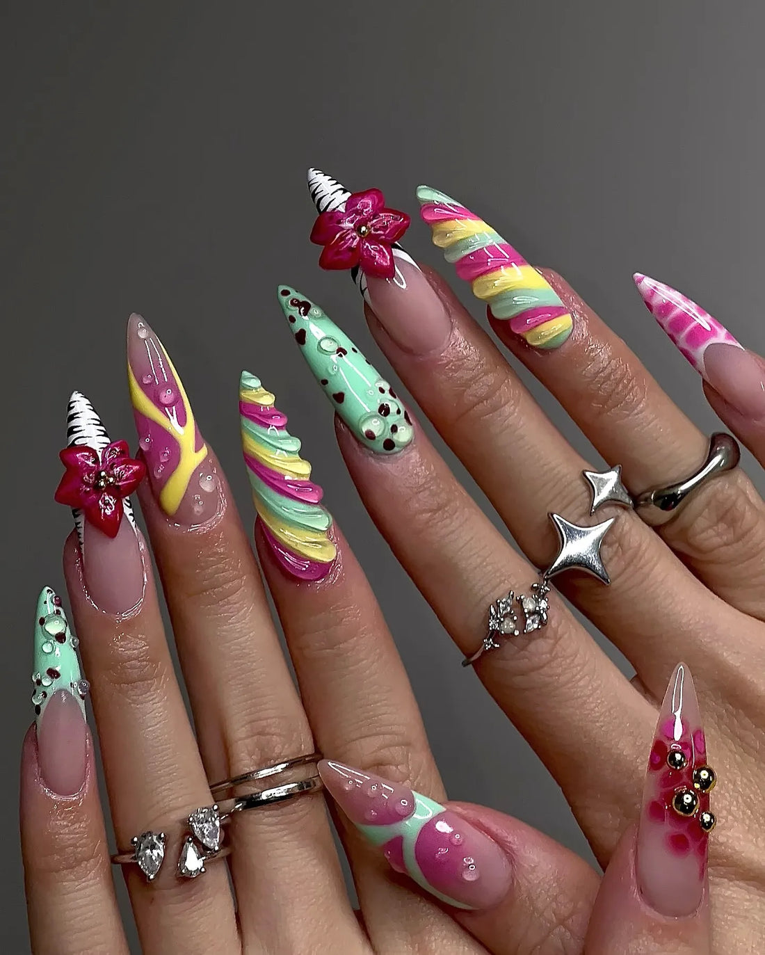 Hand with long handmade press-on nails featuring colorful candy swirl, 3D flowers, and quirky designs.