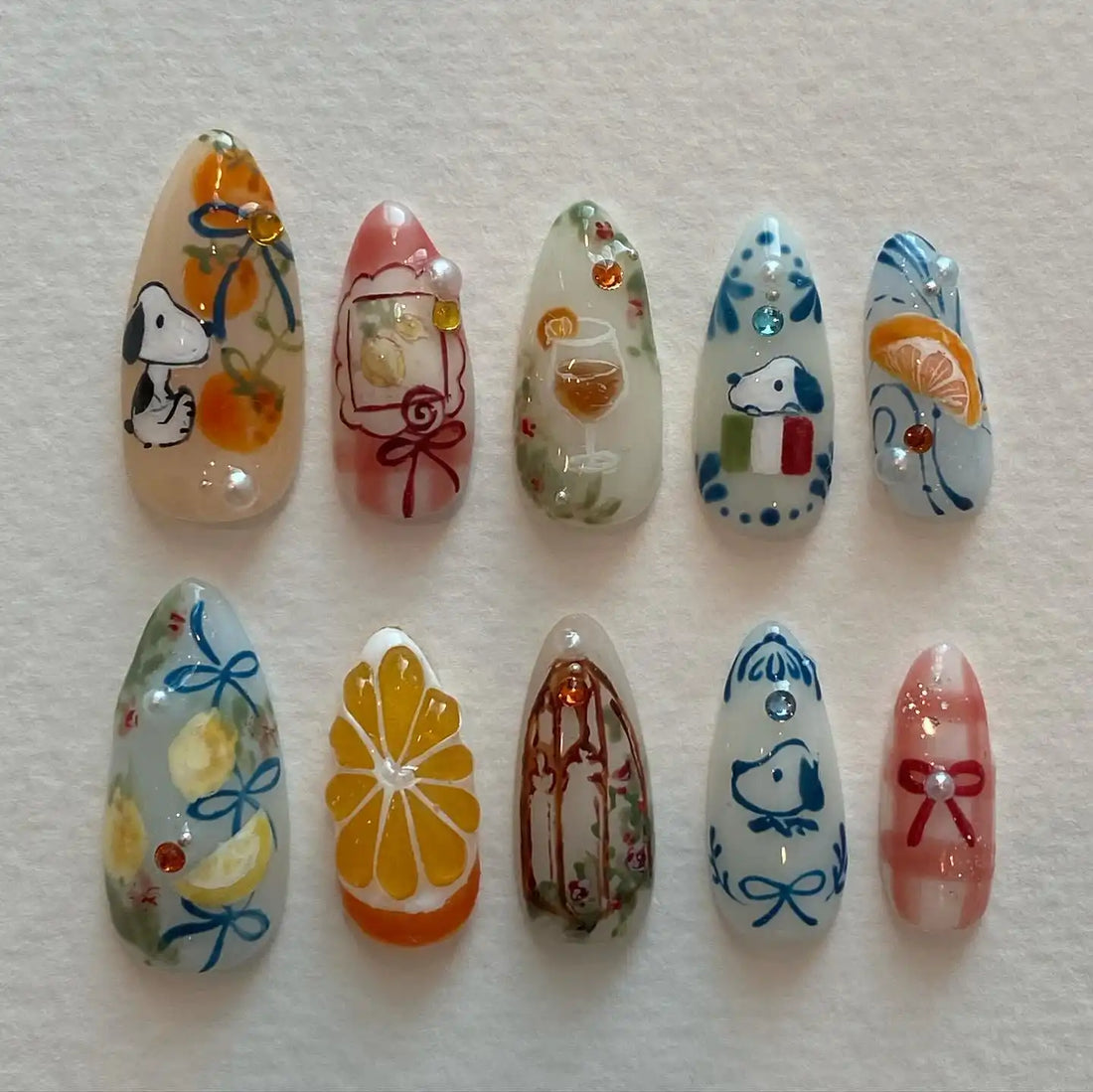 Handmade press-on nails with cartoon dog, citrus fruit, wine glass, and ribbon designs.