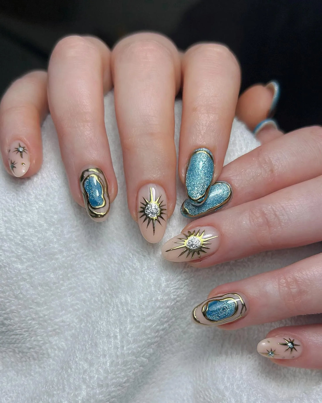 Handmade celestial press-on nails with blue shimmer, gold starburst, and constellation designs.