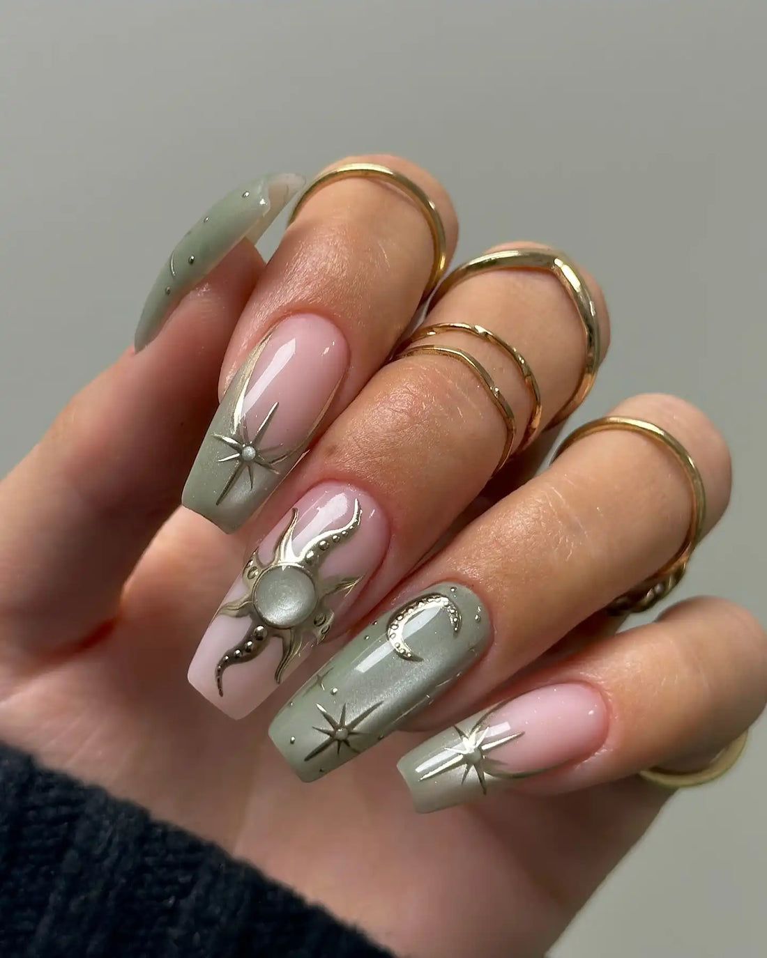 Hand holding celestial green press-on nails with gold star, moon, and sun designs
