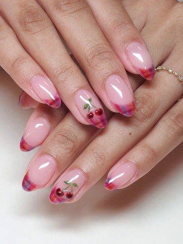 Hand with pink almond-shaped press-on nails featuring plaid French tips and cherry fruit nail art.