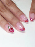 Hand with handmade press-on nails, pink plaid French tips, and cherry fruit nail art design.