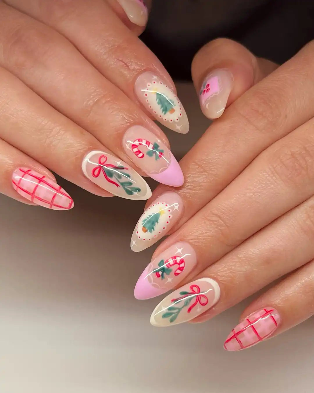Handmade press-on nails with Christmas plaid, candy cane, and tree designs in pink and green.