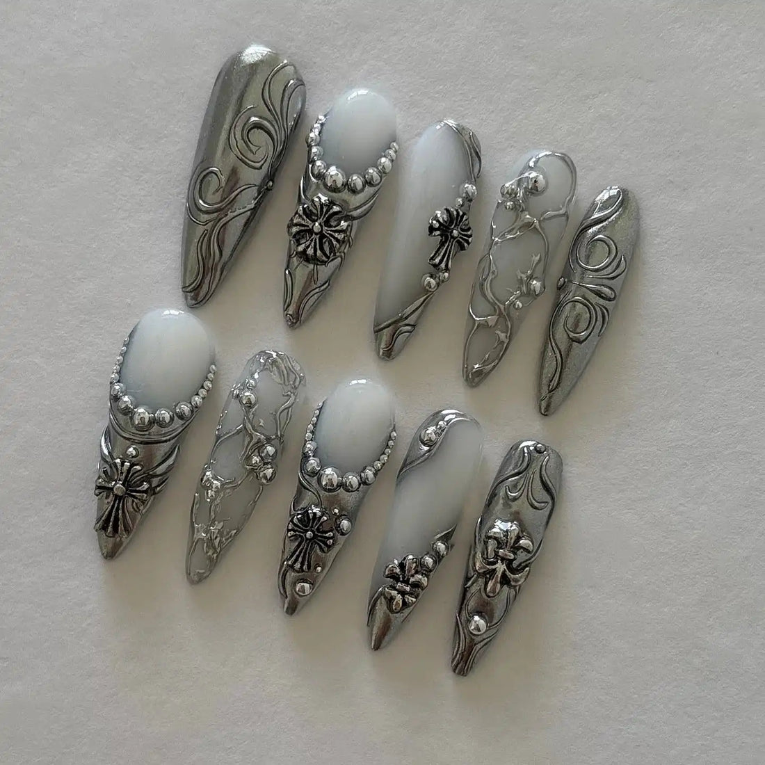 Handmade chrome silver press-on nails with gothic cross and scrollwork designs on white background