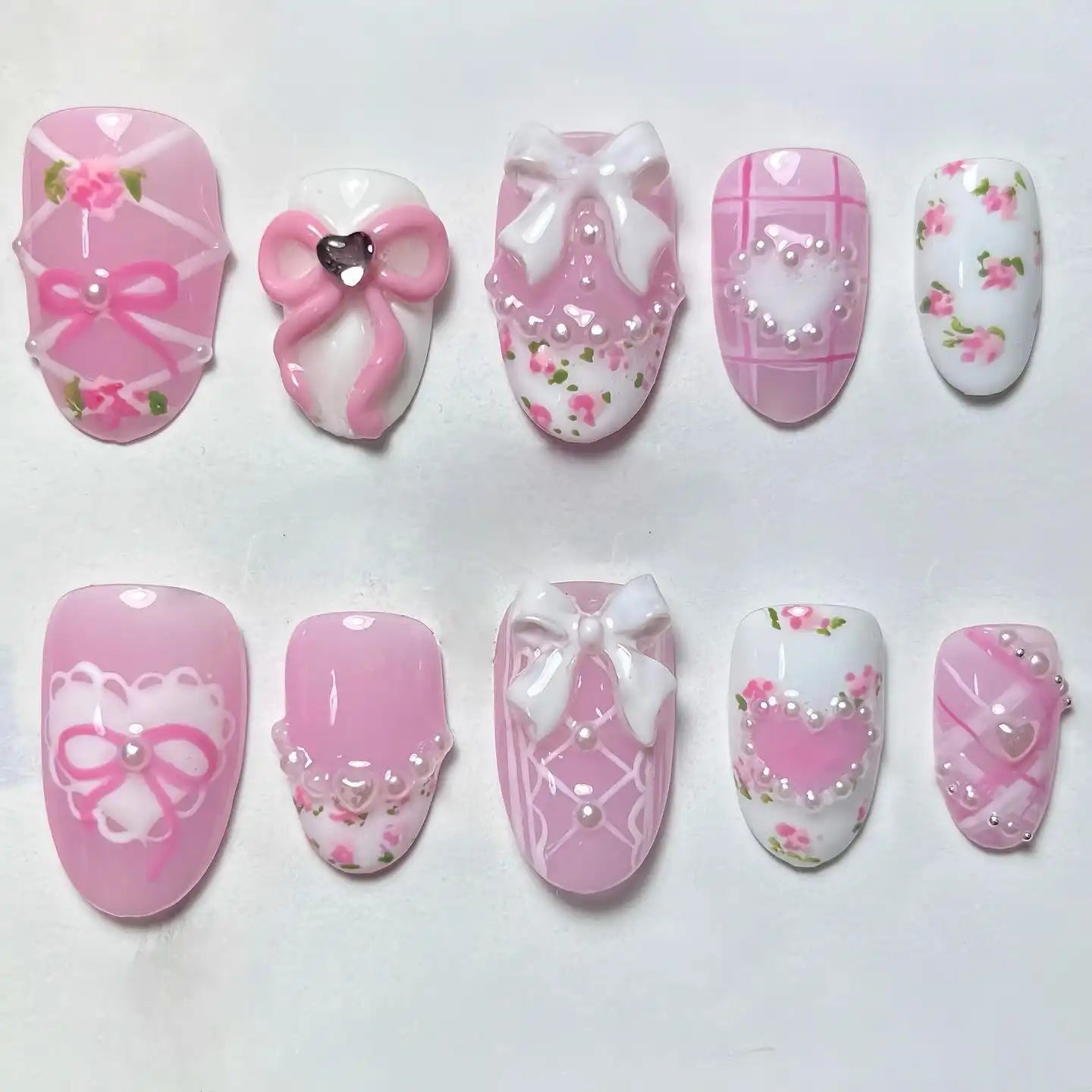 Handmade pink press-on nails with floral designs, bows, pearls, lace, and heart accents.