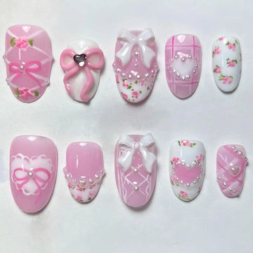 Handmade pink press-on nails with floral designs, bows, pearls, lace, and heart accents.