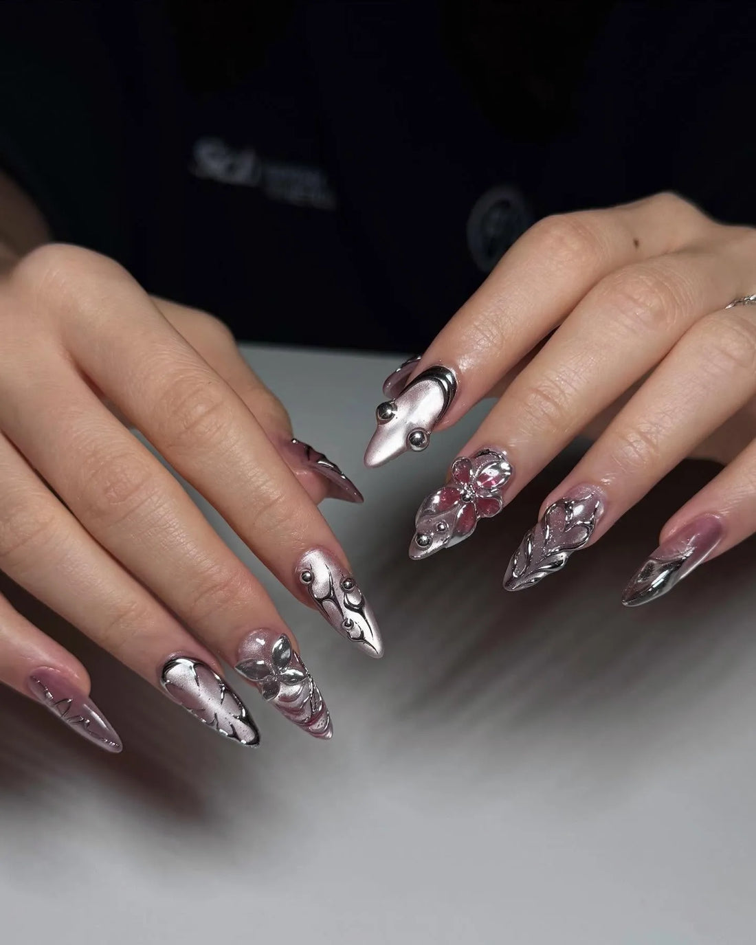 Hand with long stiletto press-on nails featuring chrome pink metallic 3D floral designs