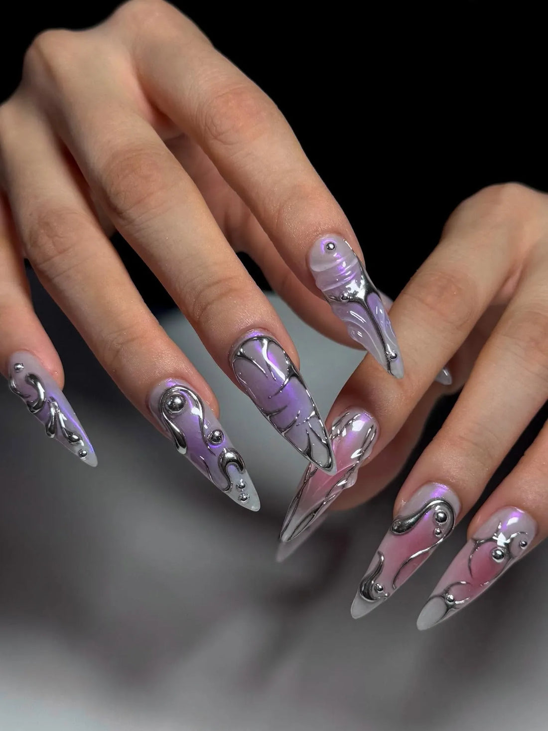 Hand with long coffin-shaped press-on nails in metallic lavender ombre, silver chrome cyberpunk design