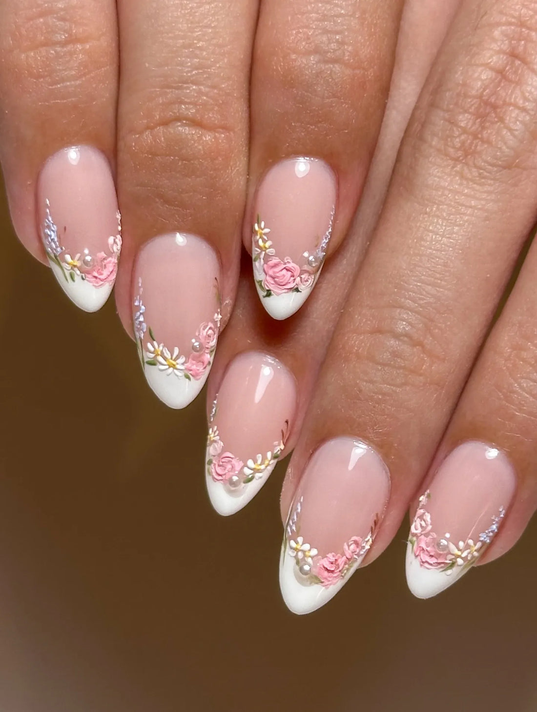 Handmade pink floral French tip press-on nails with pearl accents on natural hands