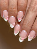 Handmade pink floral French tip press-on nails with pearl accents on natural hands