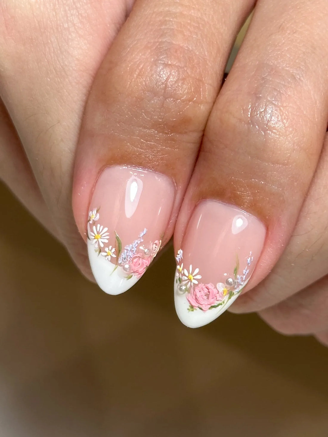 Handmade pink floral French tip press-on nails with pearl accents on natural hands