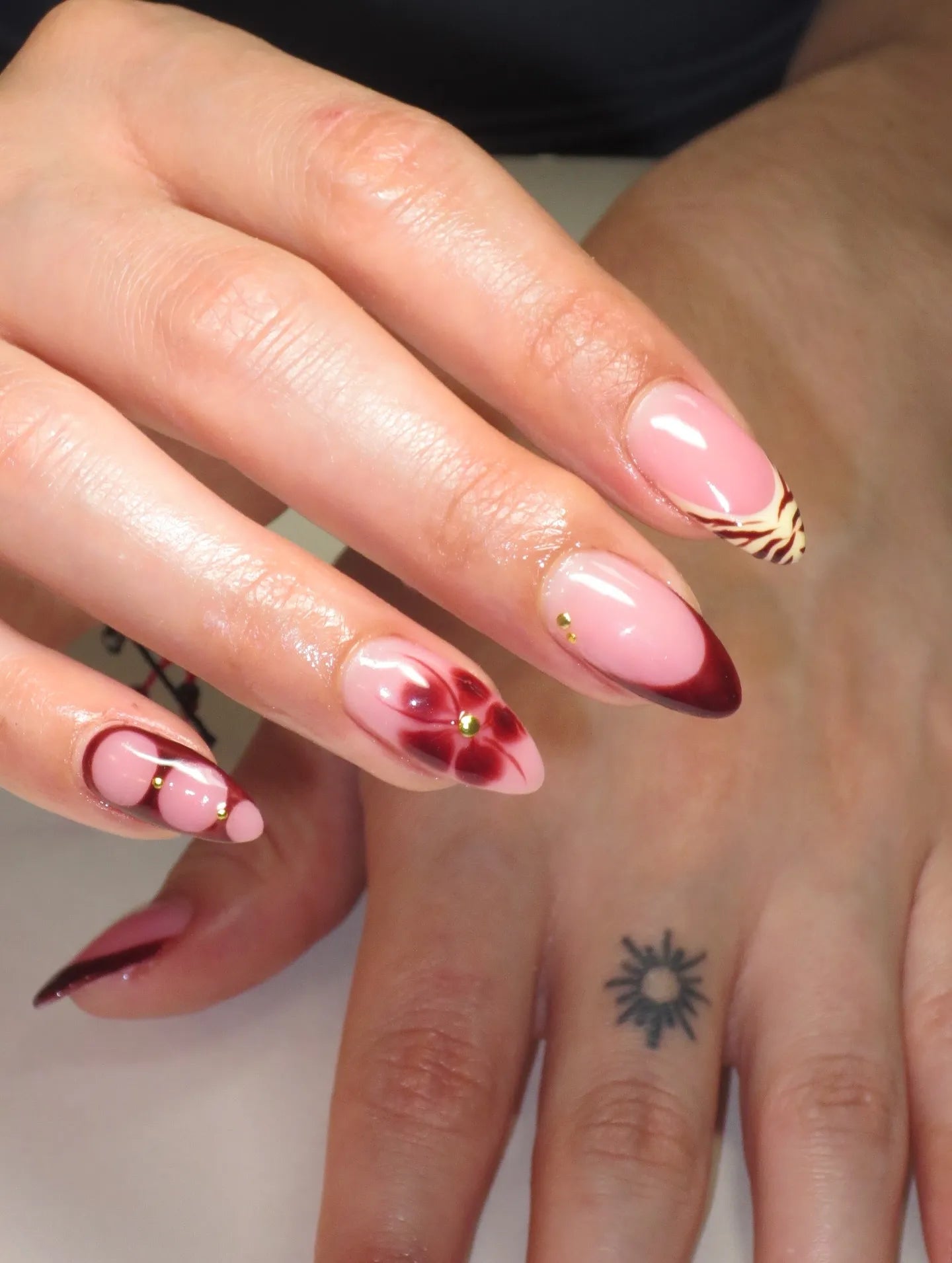 Hand with almond-shaped press-on nails, pink base, floral, tiger print, and French tip designs.
