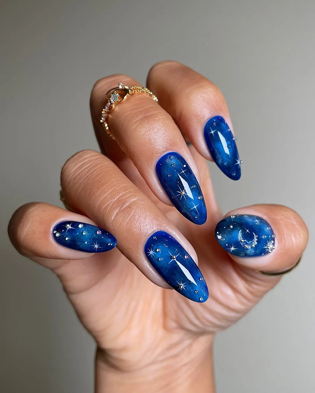 Hand with deep blue galaxy press-on nails featuring sparkling stars and moon designs.