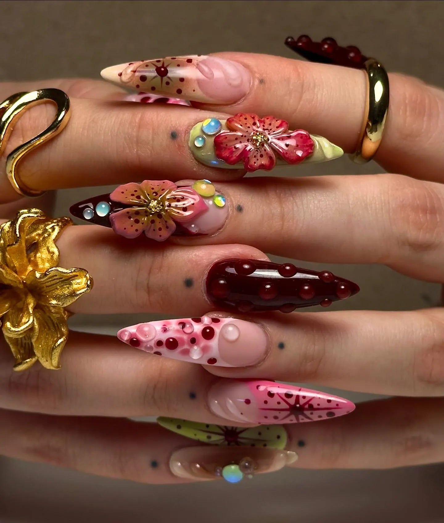 Hand with handmade deep red press-on nails featuring 3D floral designs and gemstone accents.