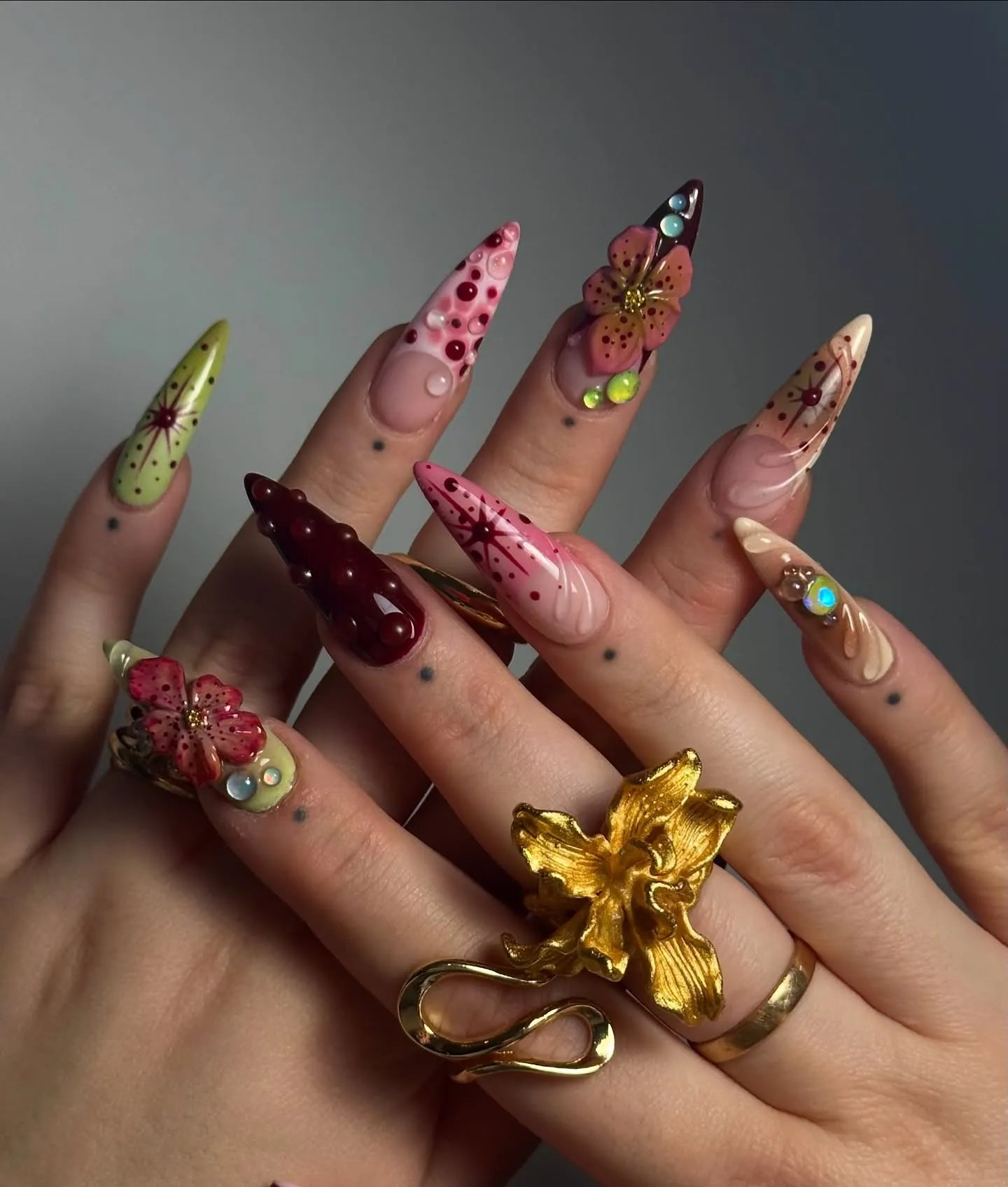 Hand with long handmade press-on nails featuring deep red 3D floral and gemstone designs.