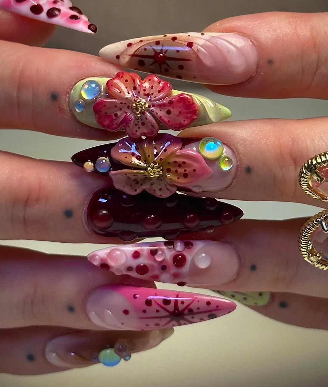 Hand with handmade deep red press-on nails featuring 3D floral designs and gemstone accents.