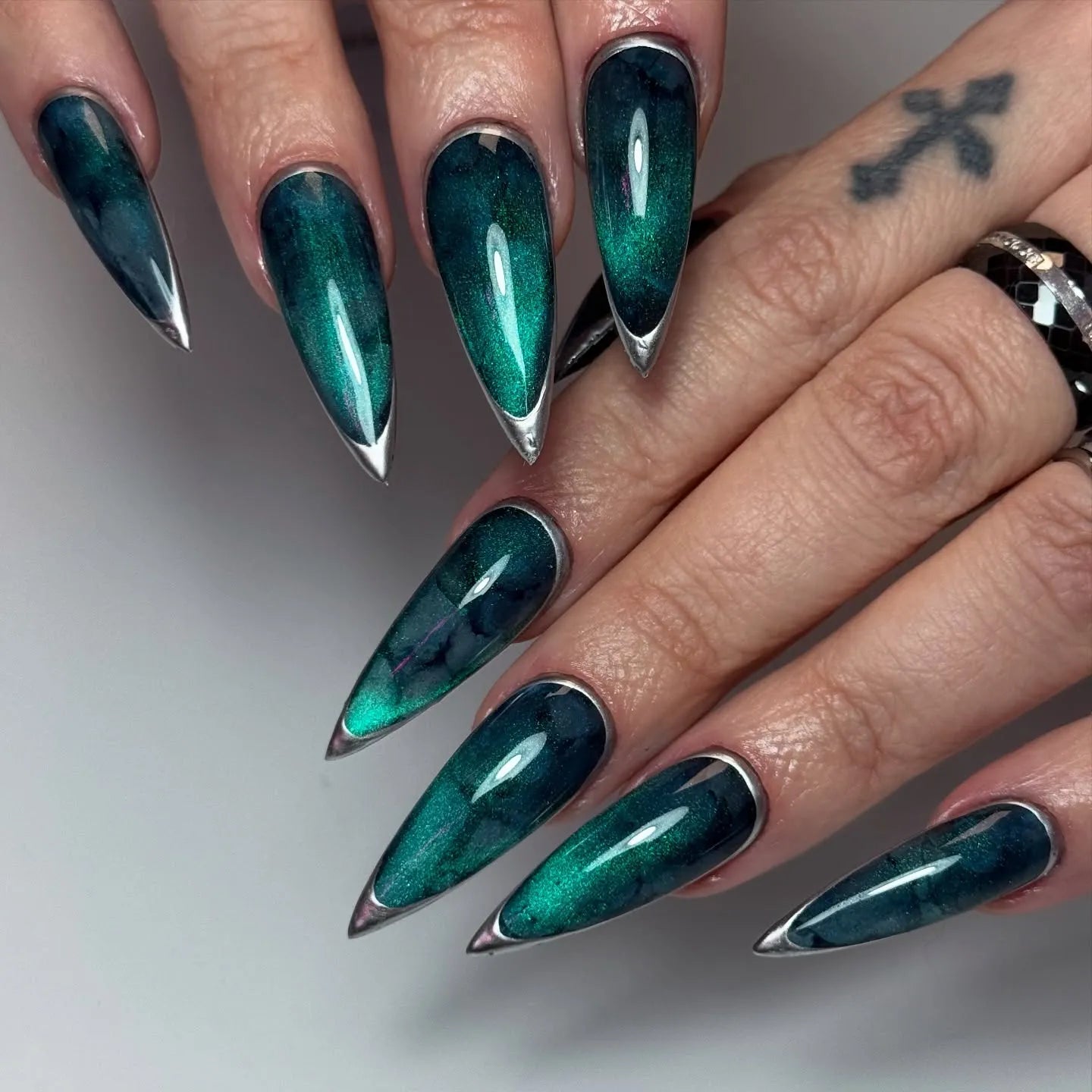 Hand with long stiletto press-on nails in deep teal nebula design with silver metallic edges