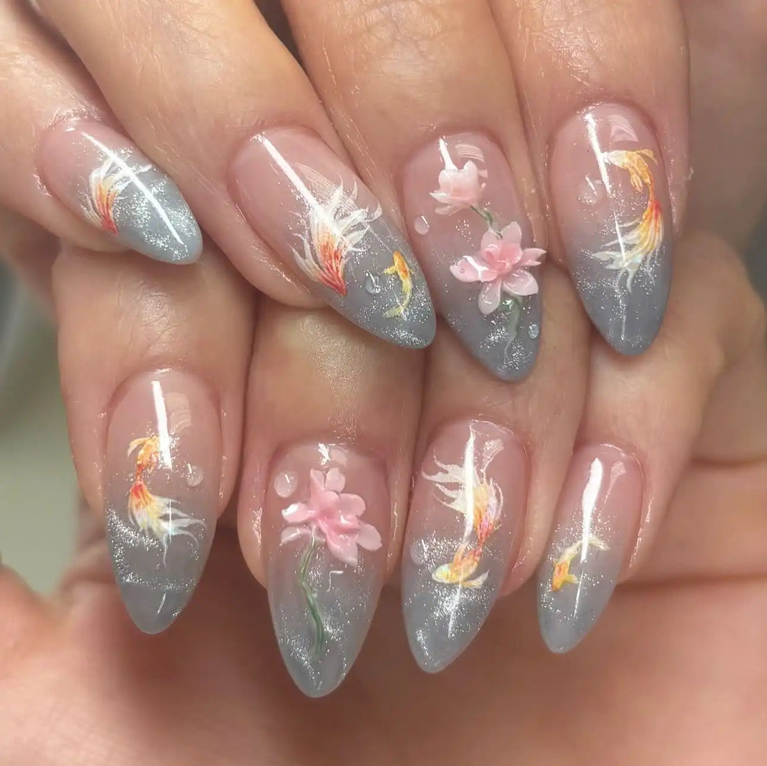 Handmade press-on nails with koi fish and pink floral designs on a gray glitter base
