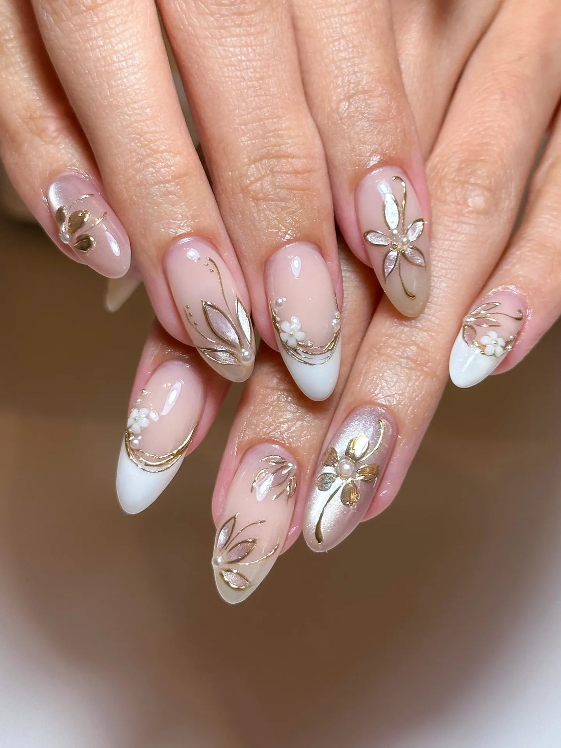 Hand with handmade gold floral metallic and pearl white French press-on nails.