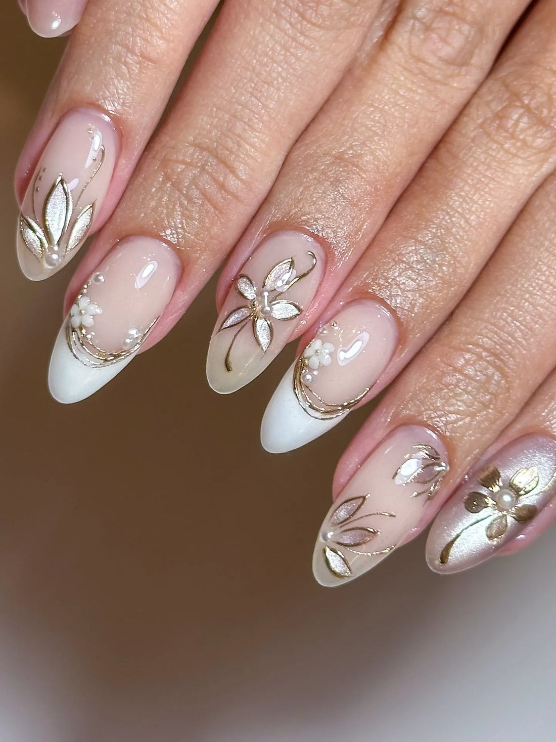 Hand with handmade gold floral metallic and pearl white French press-on nails.