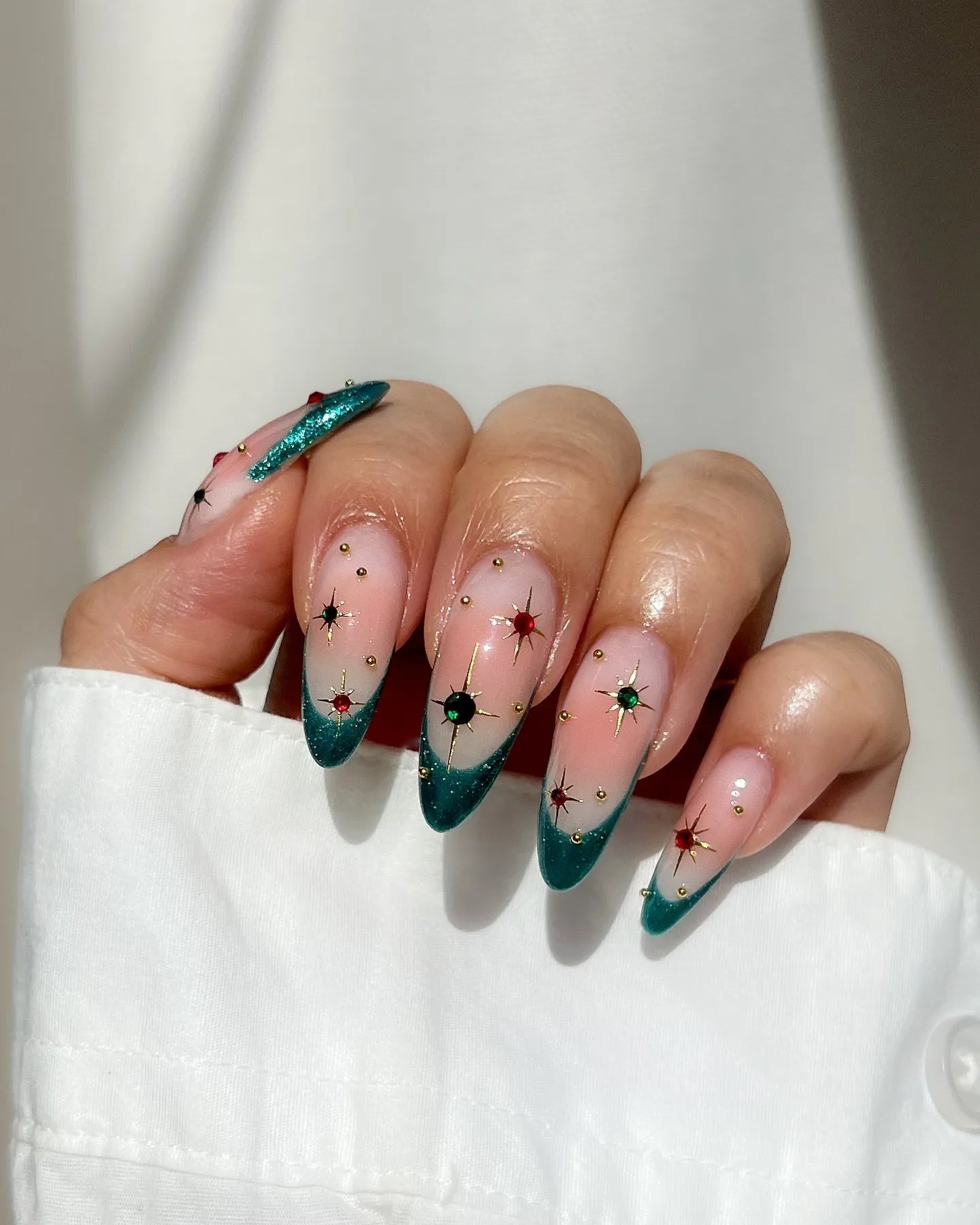 Hand with emerald green French tip press-on nails featuring gold studs and star jewel accents.
