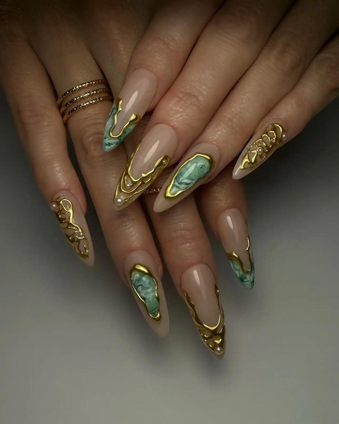 Hand with long almond-shaped press-on nails, emerald marble and gold molten designs