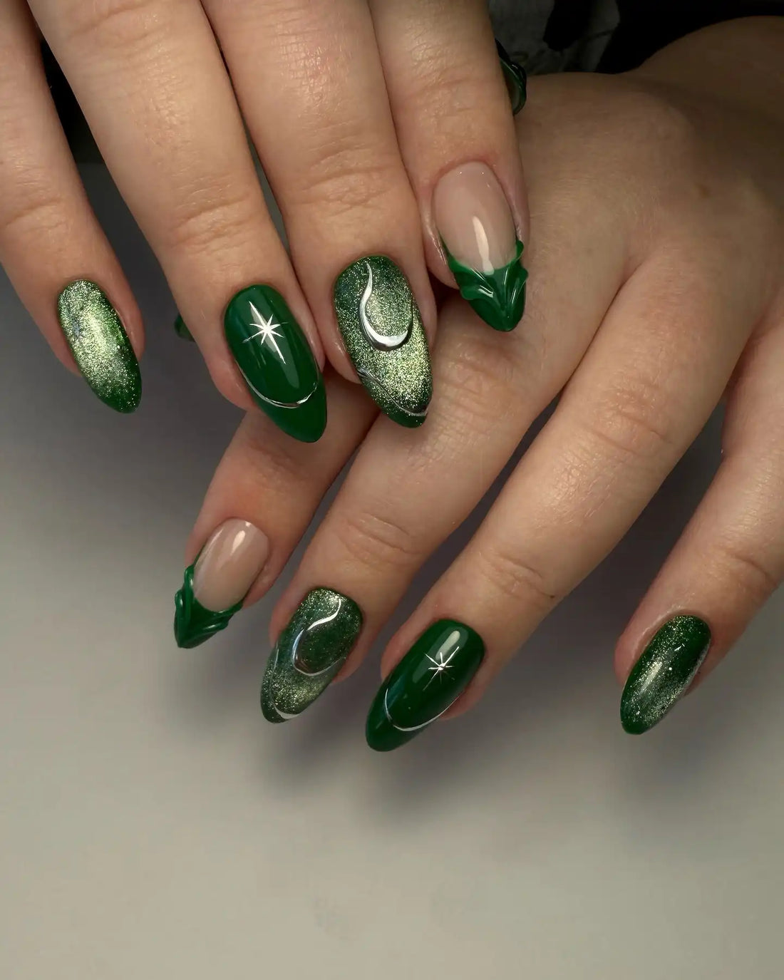 Hand with emerald green press-on nails featuring celestial moon and star designs