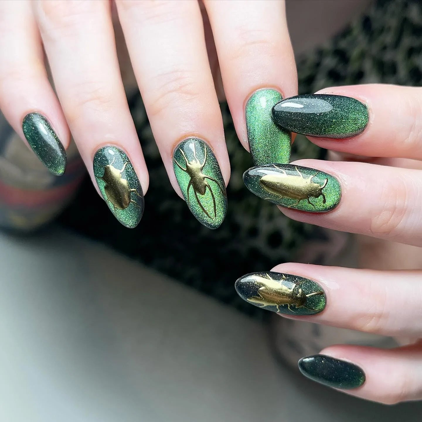 Hand with handmade oval press-on nails, green cat-eye design and gold beetle art accents